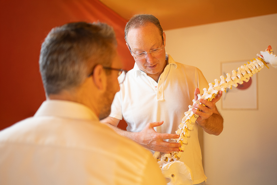 Bernhard Wilka erklärt einem Patienten anhand eines Wirbelsäulenmodells Therapieansätze und Behandlungsmöglichkeiten.